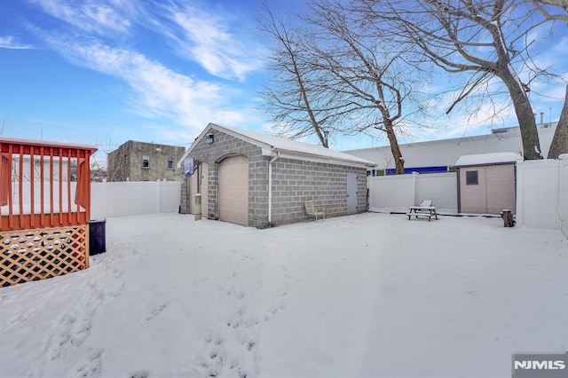 yard layered in snow featuring a shed and a garage