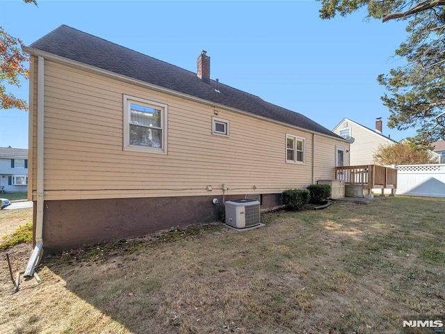 rear view of house with central AC unit and a lawn