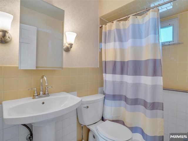 bathroom with curtained shower, sink, tasteful backsplash, toilet, and tile walls