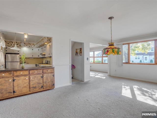 kitchen with pendant lighting, light carpet, range, white cabinetry, and stainless steel refrigerator