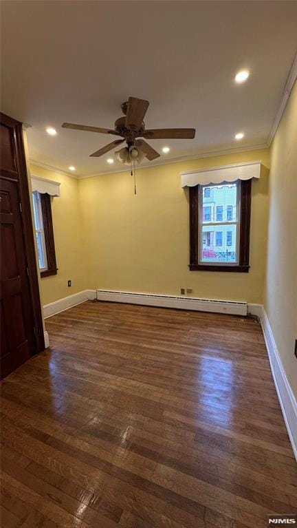 empty room featuring dark wood-type flooring, a baseboard heating unit, ceiling fan, and crown molding