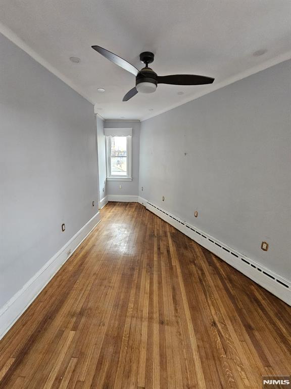 empty room with hardwood / wood-style flooring, ceiling fan, ornamental molding, and baseboard heating