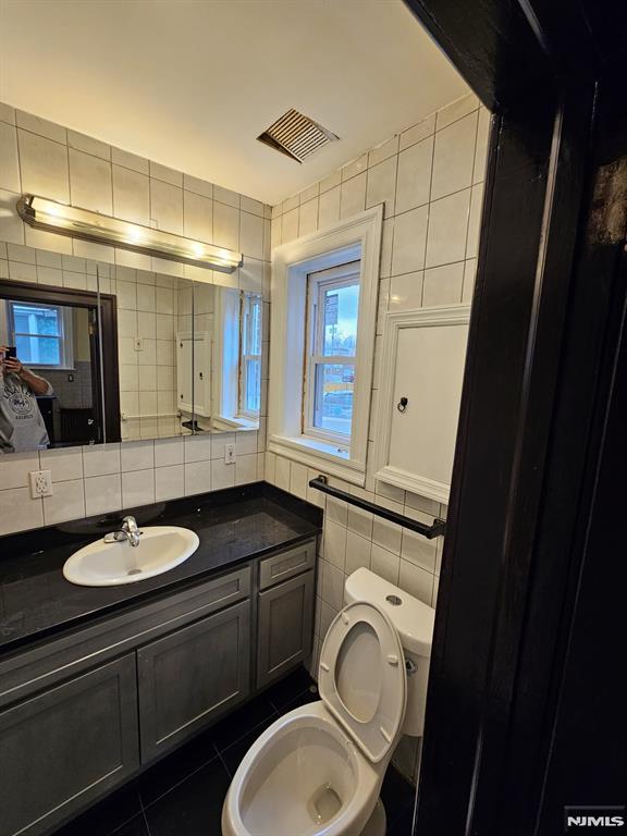 bathroom with toilet, vanity, tile patterned floors, tile walls, and decorative backsplash