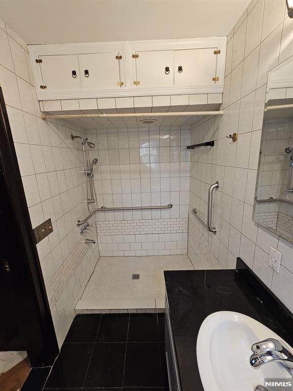 bathroom featuring sink, a tile shower, tile walls, and tile patterned floors