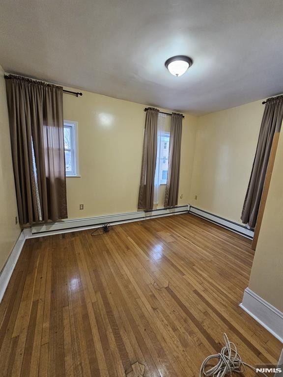 unfurnished room with a baseboard heating unit and wood-type flooring