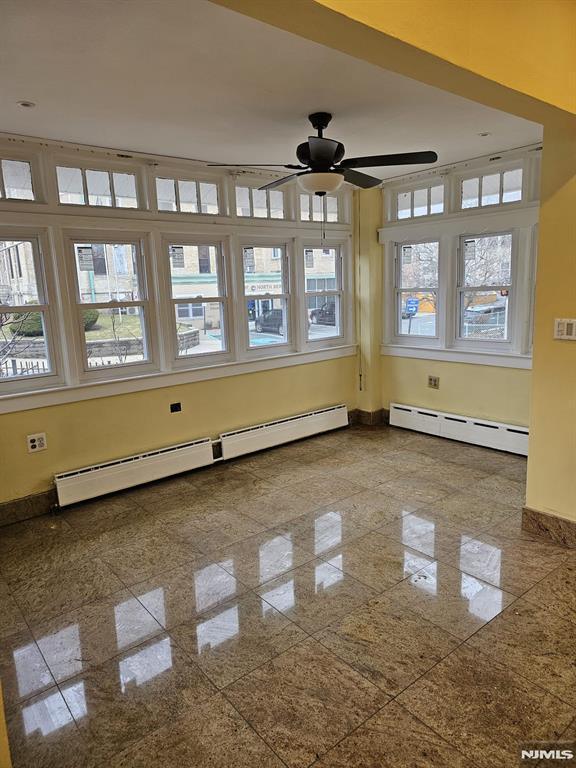 empty room featuring a baseboard radiator, ceiling fan, and plenty of natural light