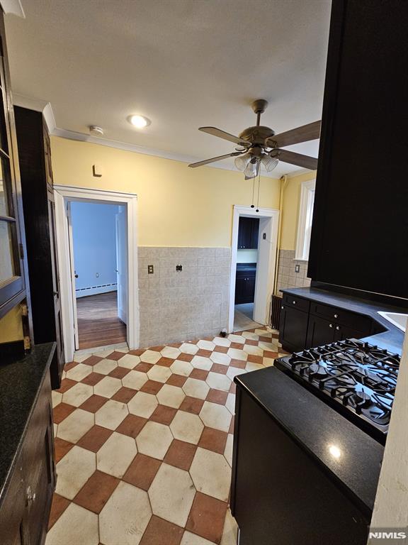 kitchen with ceiling fan, ornamental molding, tile walls, and a baseboard heating unit