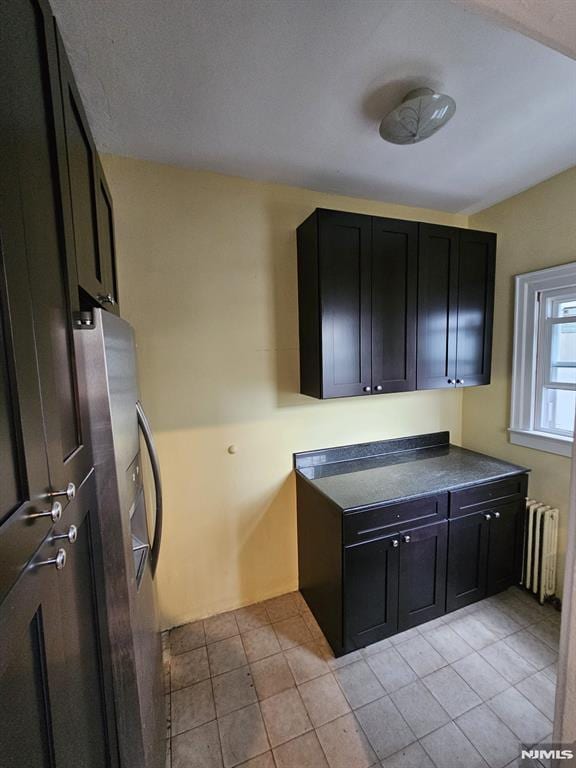 kitchen featuring light tile patterned floors, stainless steel refrigerator with ice dispenser, and radiator