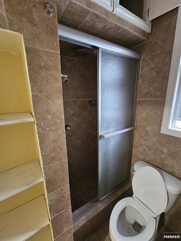 bathroom featuring tile walls, a shower with door, and toilet