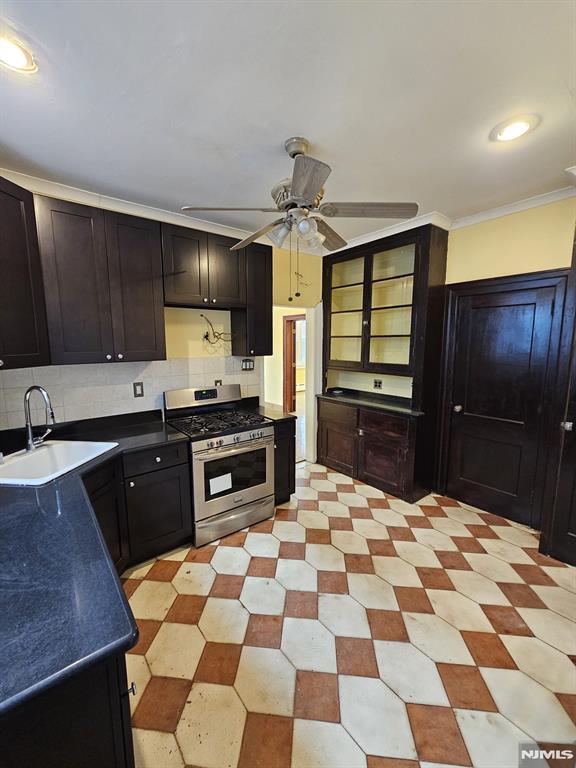 kitchen with sink, stainless steel gas range, ceiling fan, decorative backsplash, and crown molding