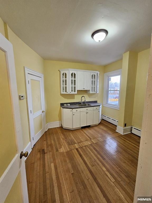 kitchen featuring sink, a baseboard heating unit, hardwood / wood-style flooring, and white cabinetry