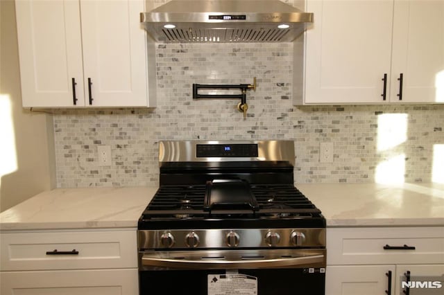 kitchen featuring gas stove, decorative backsplash, white cabinetry, and ventilation hood