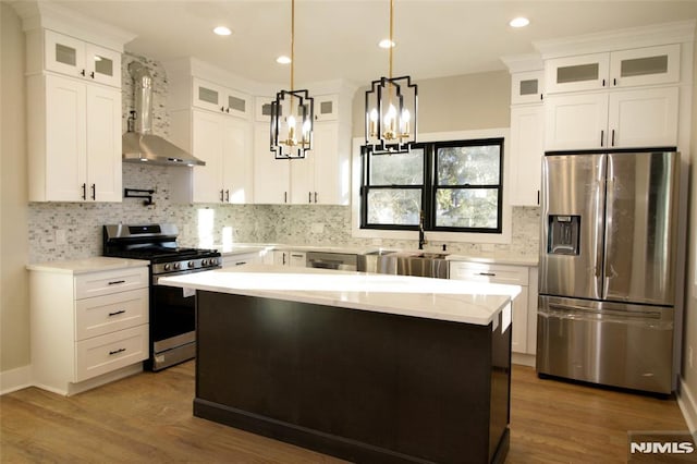 kitchen featuring stainless steel appliances, wall chimney range hood, white cabinets, a kitchen island, and hanging light fixtures