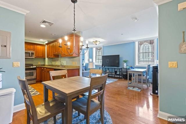 dining space featuring light wood-type flooring, crown molding, a chandelier, and sink