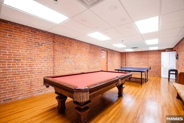 rec room featuring a paneled ceiling, light hardwood / wood-style flooring, billiards, and brick wall