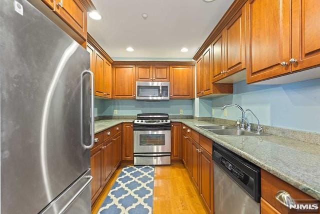 kitchen featuring appliances with stainless steel finishes, light hardwood / wood-style floors, light stone countertops, and sink