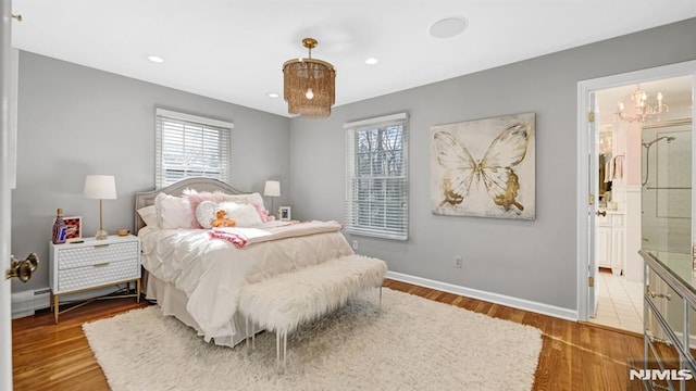 bedroom featuring a baseboard heating unit, connected bathroom, a chandelier, and wood-type flooring