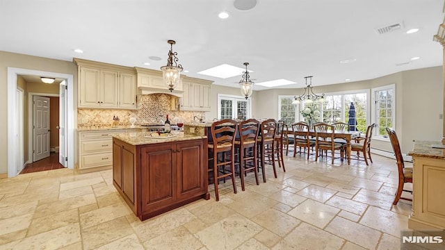 kitchen with light stone countertops, cream cabinets, pendant lighting, a kitchen island, and a skylight