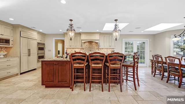 kitchen featuring a skylight, cream cabinets, decorative light fixtures, and light stone counters