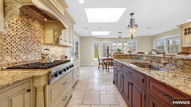 kitchen featuring a skylight, stainless steel gas stovetop, sink, decorative light fixtures, and backsplash