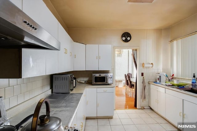 kitchen featuring backsplash, white cabinetry, exhaust hood, and light tile patterned floors