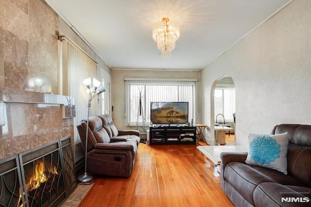 living room with hardwood / wood-style flooring, a notable chandelier, crown molding, and a tile fireplace