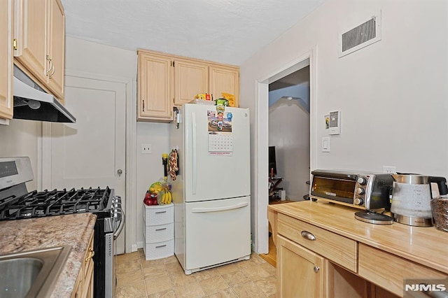 kitchen with white refrigerator, light brown cabinets, and gas range