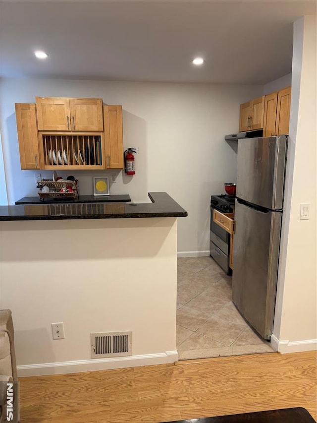 kitchen featuring appliances with stainless steel finishes, dark stone countertops, kitchen peninsula, and light tile patterned floors