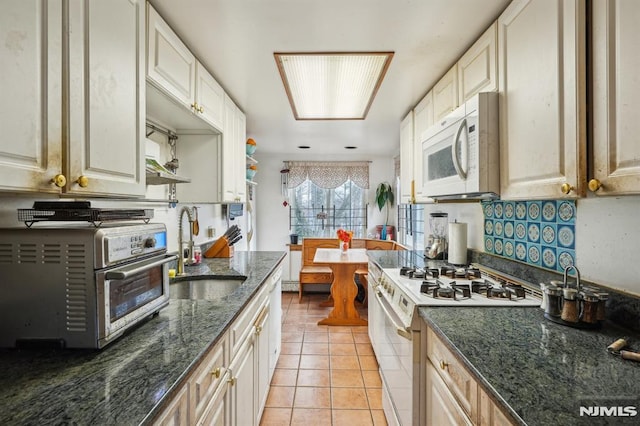 kitchen with white appliances, dark stone counters, sink, and light tile patterned floors