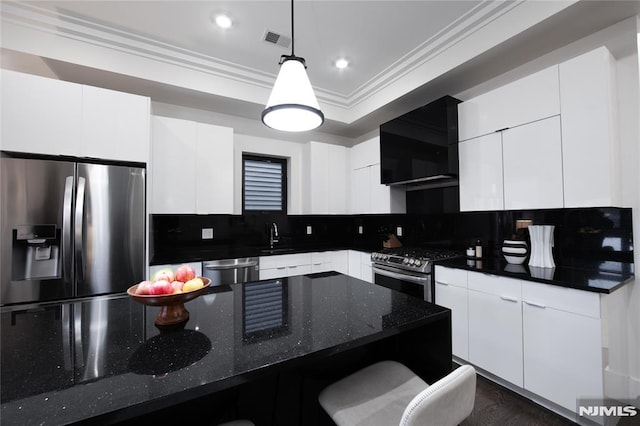 kitchen featuring tasteful backsplash, wall chimney range hood, pendant lighting, appliances with stainless steel finishes, and white cabinets