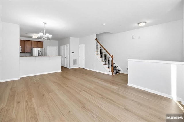 unfurnished living room with light wood-type flooring and a notable chandelier