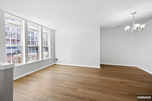 unfurnished room with a notable chandelier, plenty of natural light, and wood-type flooring