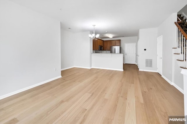 unfurnished living room featuring an inviting chandelier and light wood-type flooring