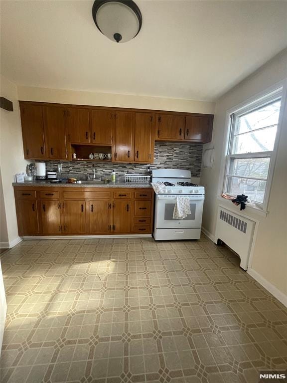 kitchen with backsplash, white range with gas stovetop, radiator, and sink