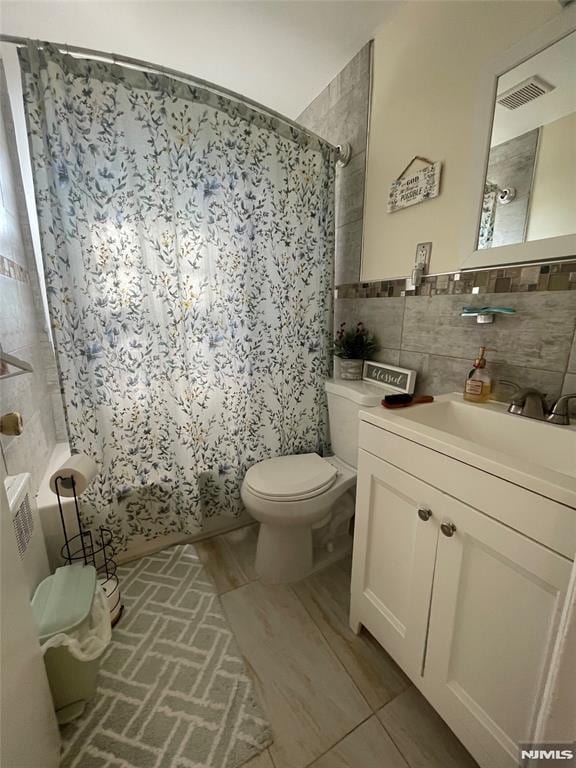 full bathroom featuring toilet, shower / bath combo with shower curtain, decorative backsplash, tile walls, and vanity