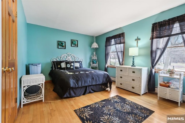 bedroom with baseboard heating, light wood-type flooring, and multiple windows