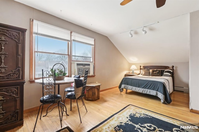 bedroom featuring vaulted ceiling, rail lighting, light wood-type flooring, ceiling fan, and a baseboard radiator