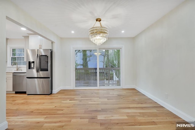 unfurnished dining area with an inviting chandelier, light hardwood / wood-style flooring, and sink