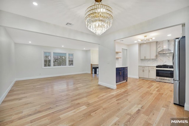 kitchen with wall chimney exhaust hood, a chandelier, decorative backsplash, white cabinetry, and appliances with stainless steel finishes