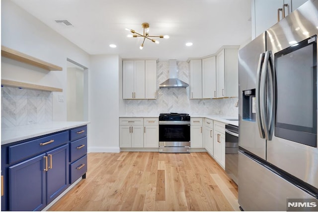 kitchen with stainless steel appliances, wall chimney exhaust hood, white cabinetry, blue cabinets, and backsplash