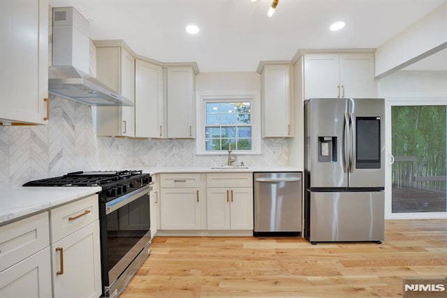 kitchen with stainless steel appliances, sink, light hardwood / wood-style flooring, light stone countertops, and wall chimney range hood