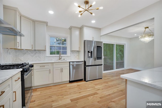 kitchen with a chandelier, appliances with stainless steel finishes, decorative backsplash, wall chimney range hood, and decorative light fixtures