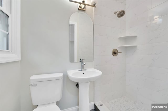 bathroom with toilet, tiled shower, and sink