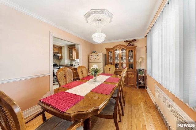 dining room featuring a notable chandelier, ornamental molding, light hardwood / wood-style flooring, and radiator heating unit