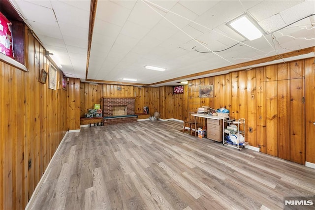 basement with a brick fireplace, light hardwood / wood-style flooring, and wooden walls