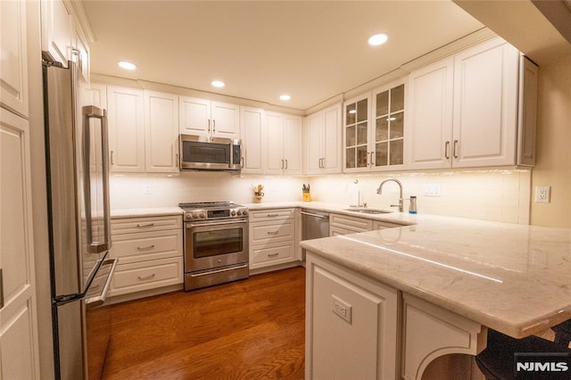 kitchen featuring light stone countertops, white cabinets, stainless steel appliances, sink, and kitchen peninsula