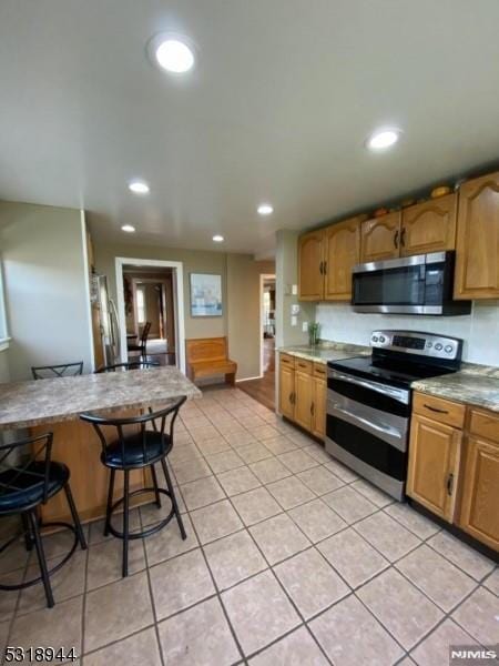 kitchen with appliances with stainless steel finishes, a breakfast bar, and light tile patterned floors