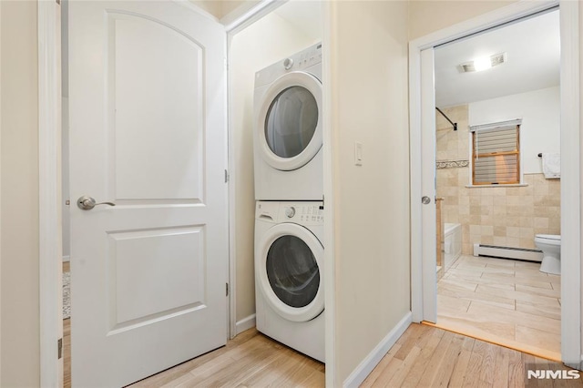 laundry area with stacked washer / drying machine, baseboard heating, and light hardwood / wood-style floors