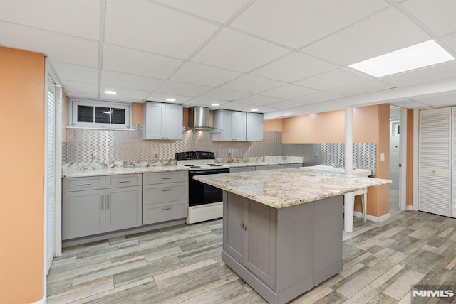 kitchen featuring wall chimney exhaust hood, tasteful backsplash, a kitchen island, gray cabinets, and white electric range