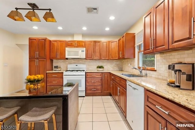 kitchen featuring white appliances, light stone countertops, light tile patterned floors, a breakfast bar area, and sink